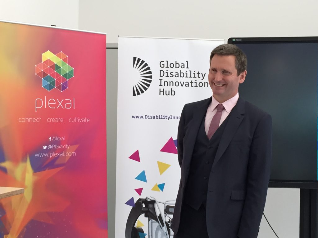 Chris in suit smiling in front of banner saying Global Disability Innovation Hub